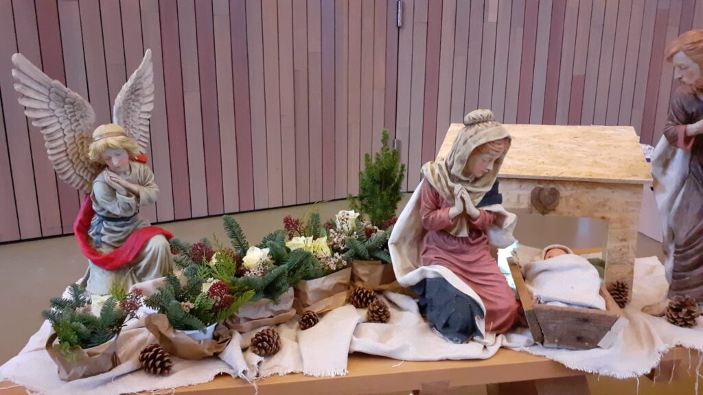 klassieke beelden van Engel, Jozef en Maria met daartussen kerststukjes en een kindje in een houten kribbe en een houten stal met een hartje boven de open deur. 