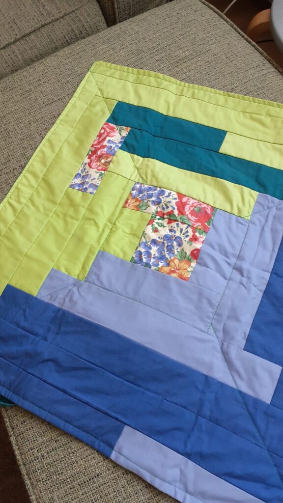 A small quilt made by Jessica, with stripes of green and blues and some colorful flower fabric. It was purposefully not made totally symmetrical. 